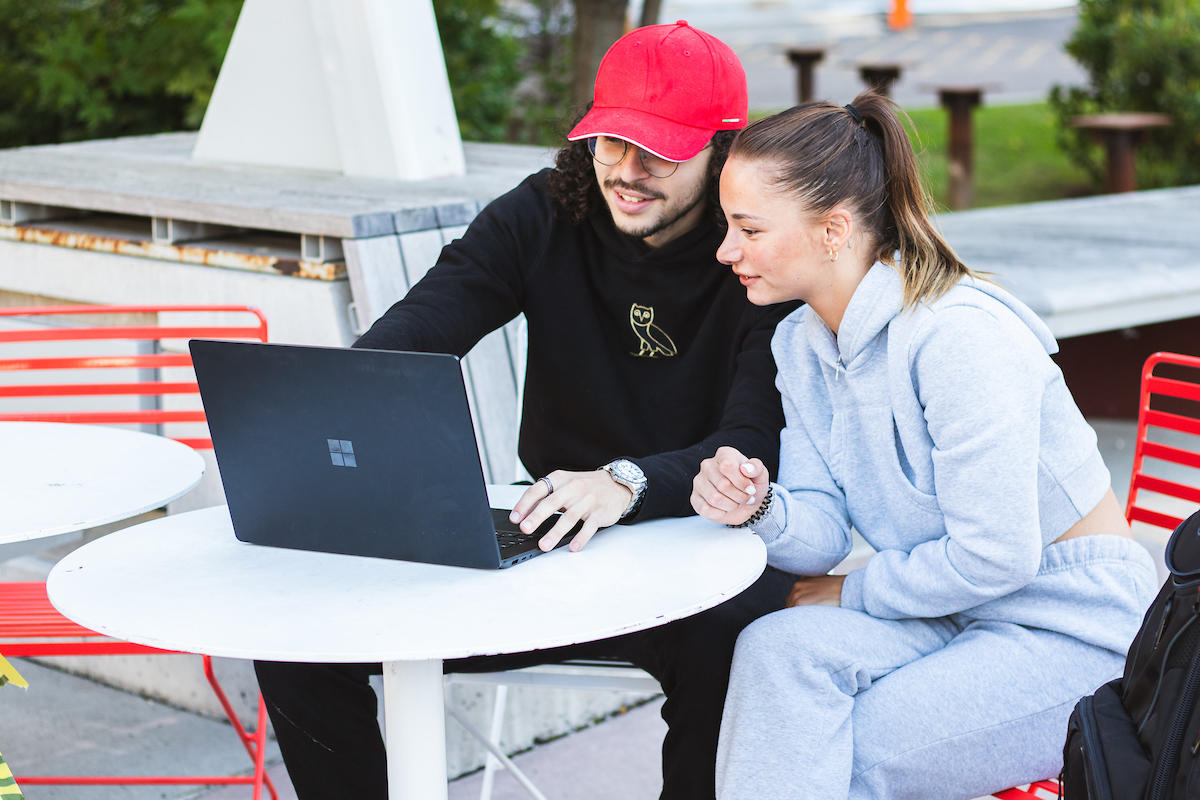 Two students outside studying on laptop.