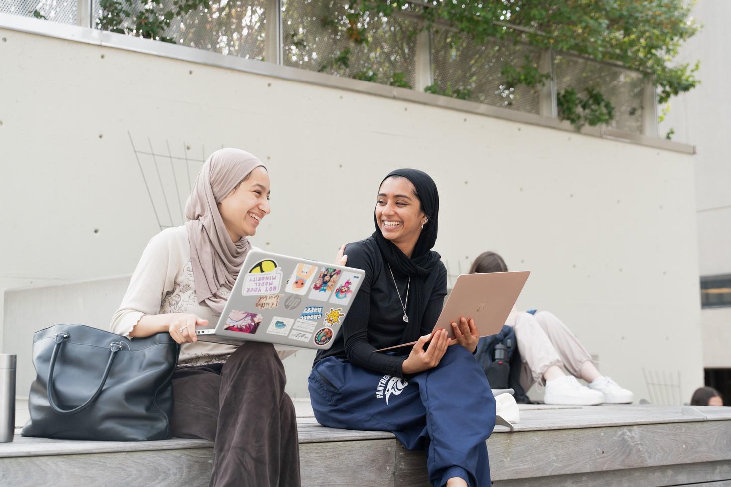 2 students sitting with their laptops on campus