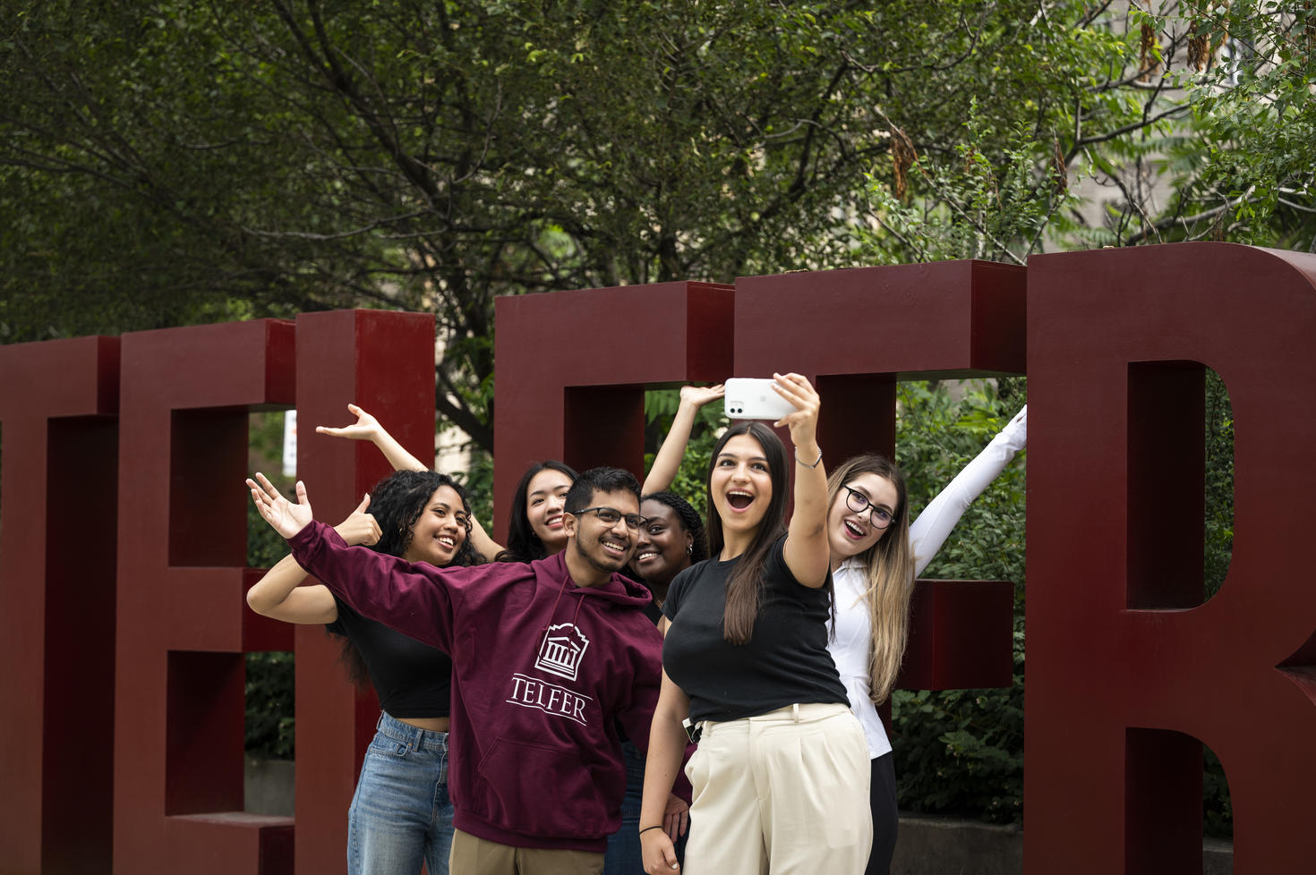 Smiling students in front of the giant “TELFER” letters on campus.