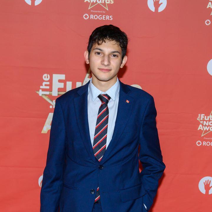Santiago Proteau-Sanchez posing in front of a red background at "The future is now award".