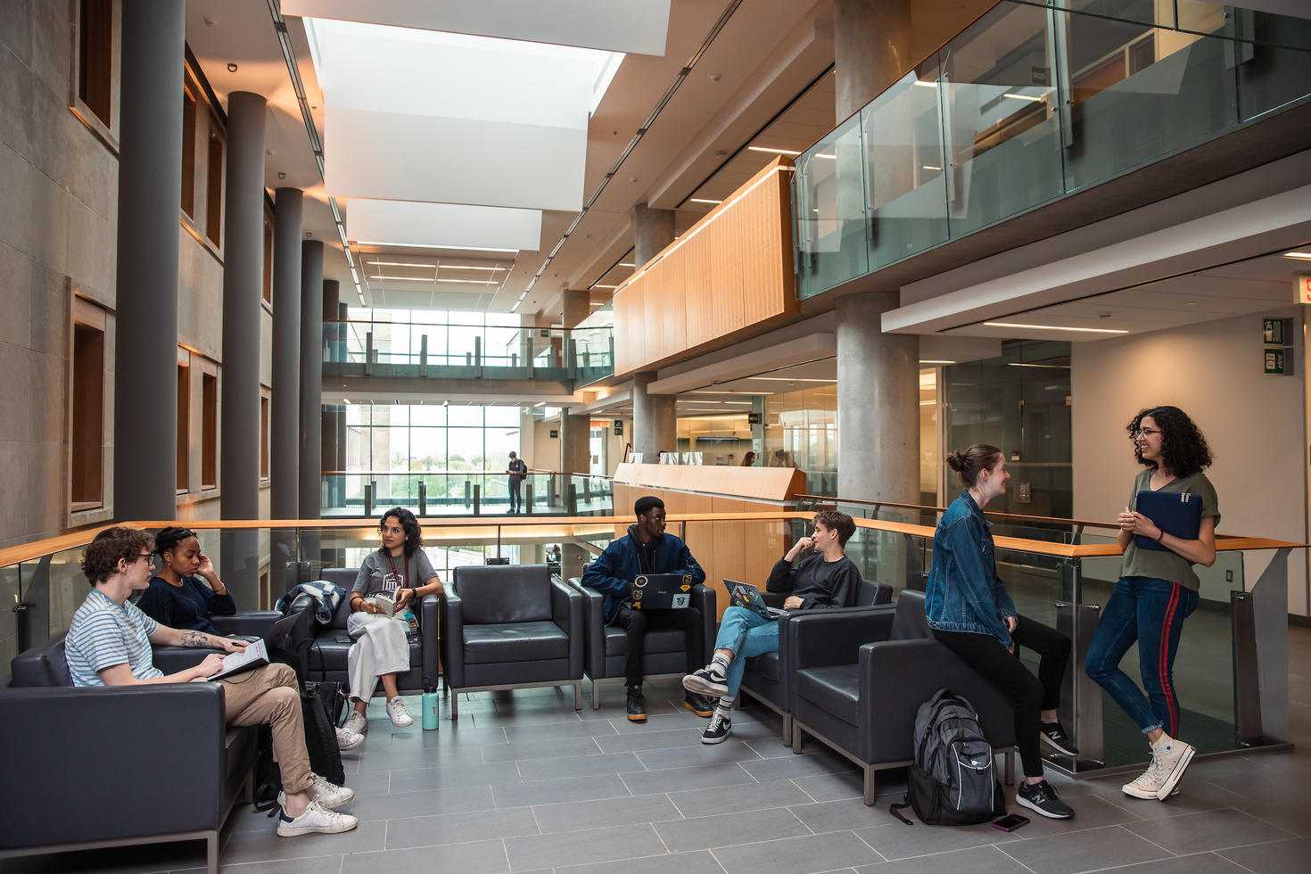 Students studying and chatting on lounge chairs in a bright atrium at the Faculty of Social Sciences.