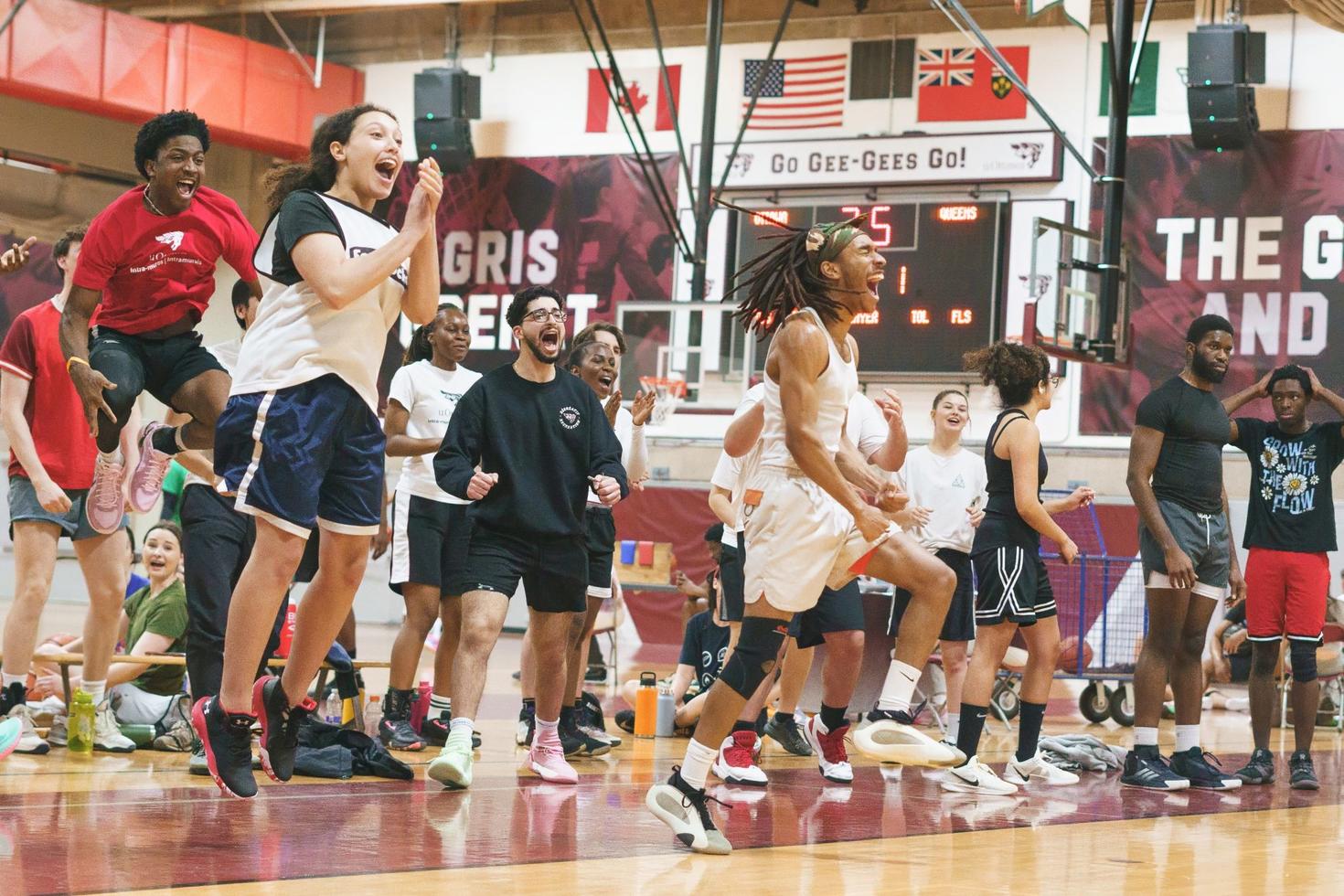 Intramurals basketball players jump with joy on the sidelines as teammates score.