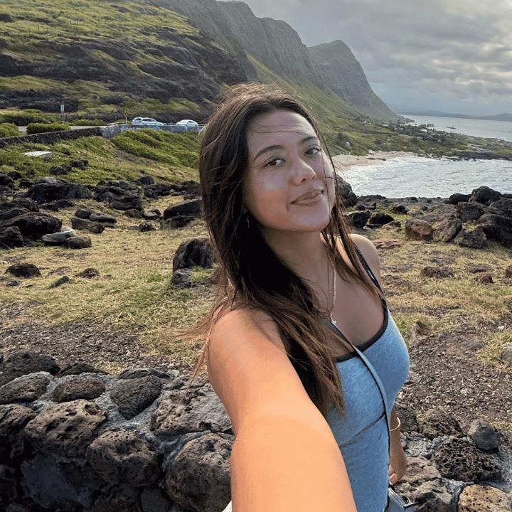 Kayla Hunkin takes a selfie in front of mountains and a bay in Hawaii.