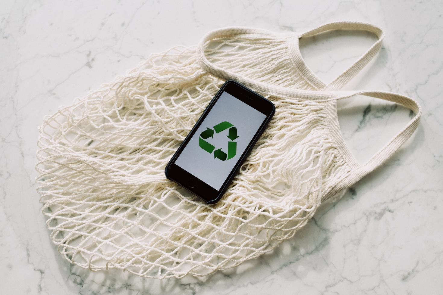 Symbole du recyclage apparaissant sur l’écran d’un téléphone cellulaire déposé sur un sac réutilisable