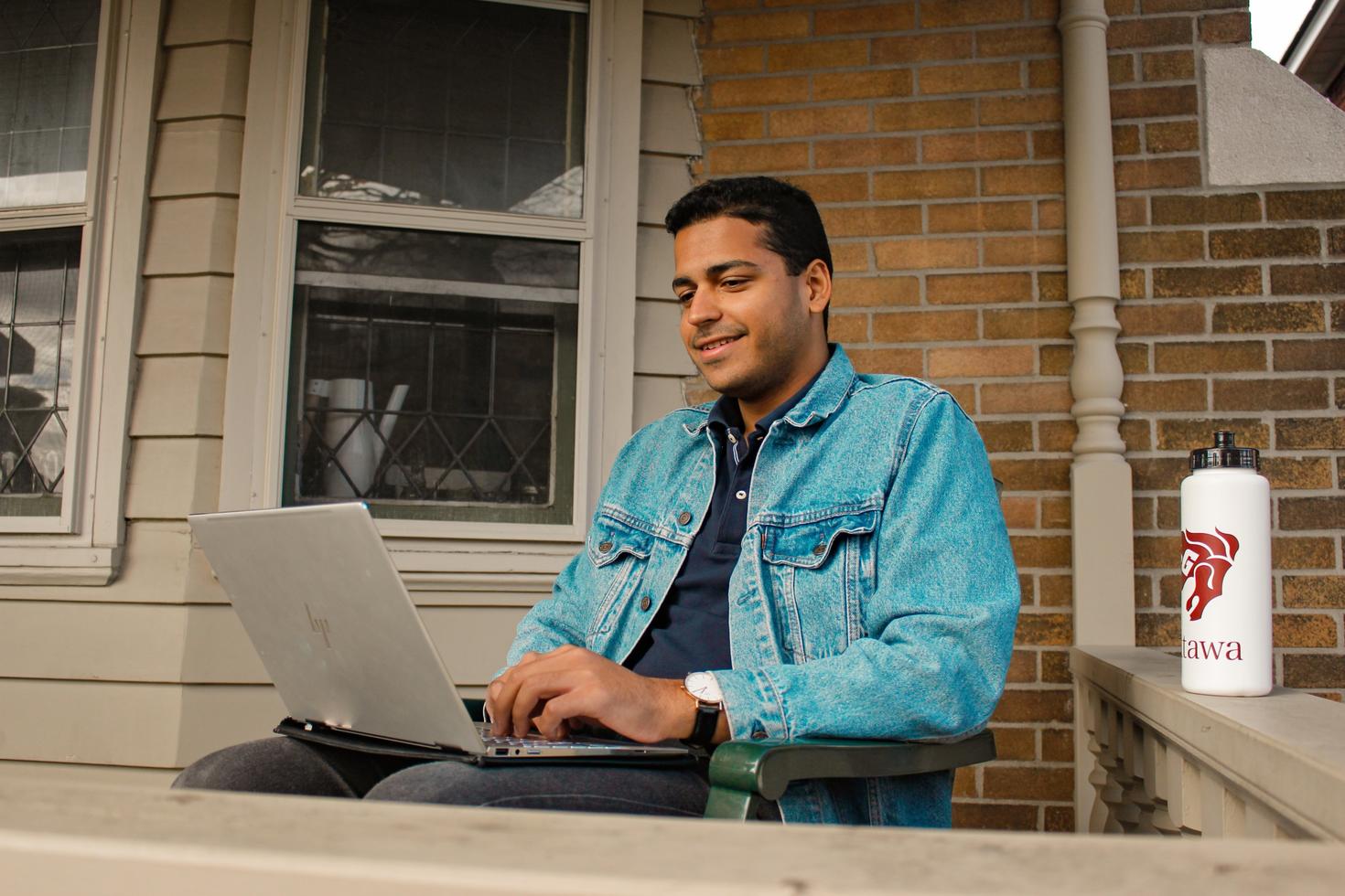 Étudiant travaillant sur son ordinateur portable sur le porche d'entrée.