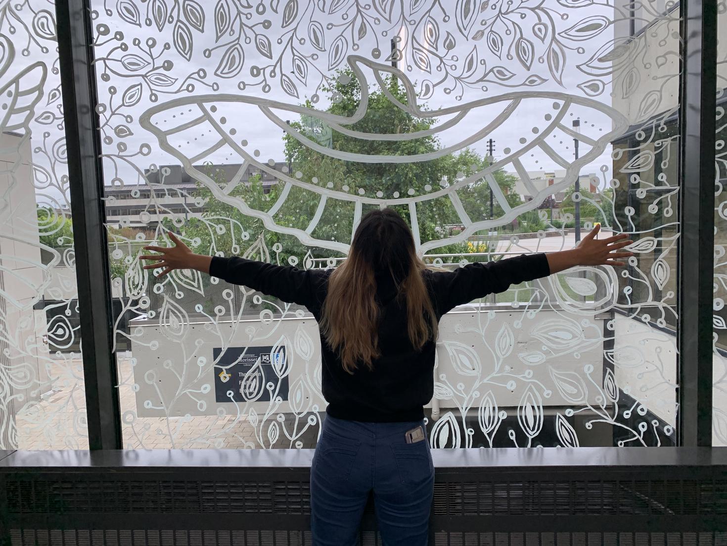 Étudiante étendant les bras devant une fresque d’oiseau dessinée dans une fenêtre