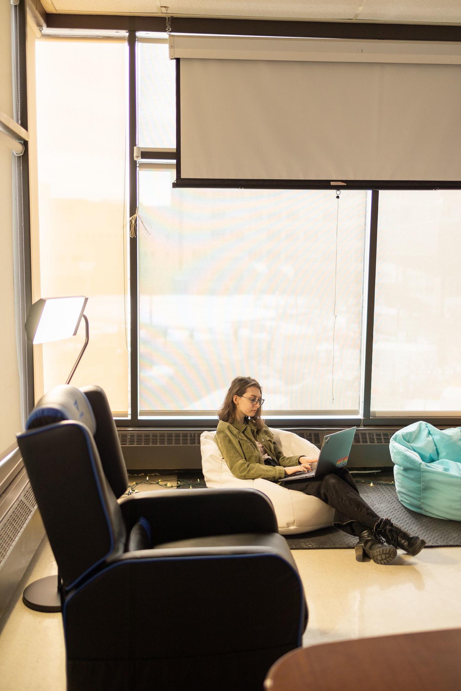 étudiante assise sur un pouf et travaillant sur son ordinateur portable