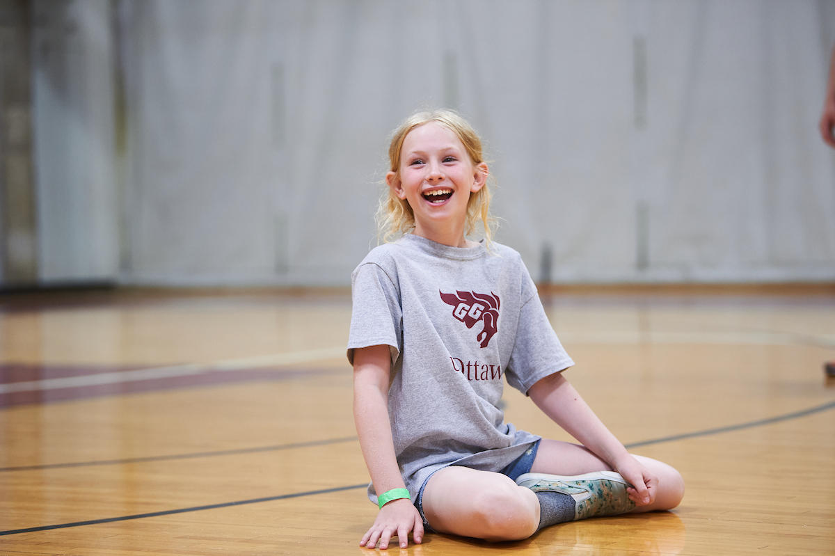 enfant assis souriant avec un T-shirt de camp