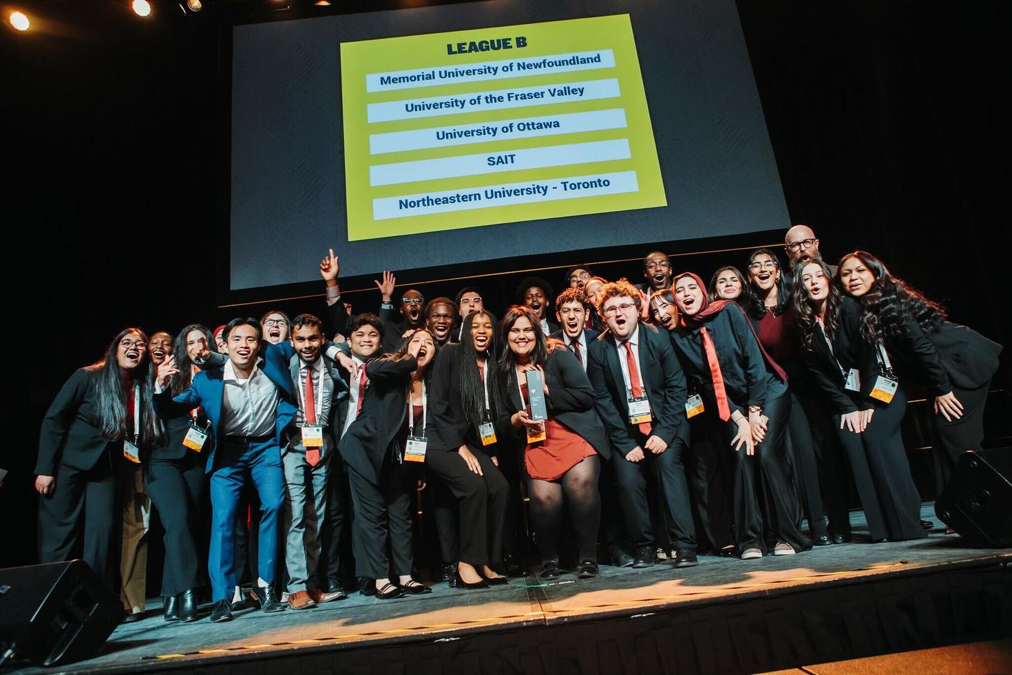 Un grand groupe d'étudiantes et étudiants de l'équipe Enactus de l'Université d'Ottawa sur scène lors d'une compétition avec d'autres universités.