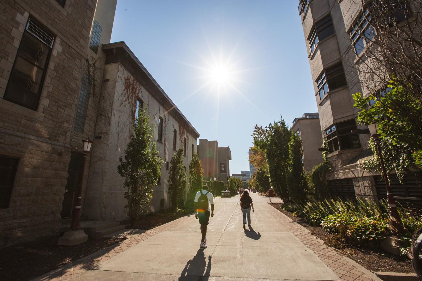 Deux étudiants marchent vers le soleil éclatant le long de la Grande Allée | Kichi Mìkàns, sur le campus de l'Université d'Ottawa.