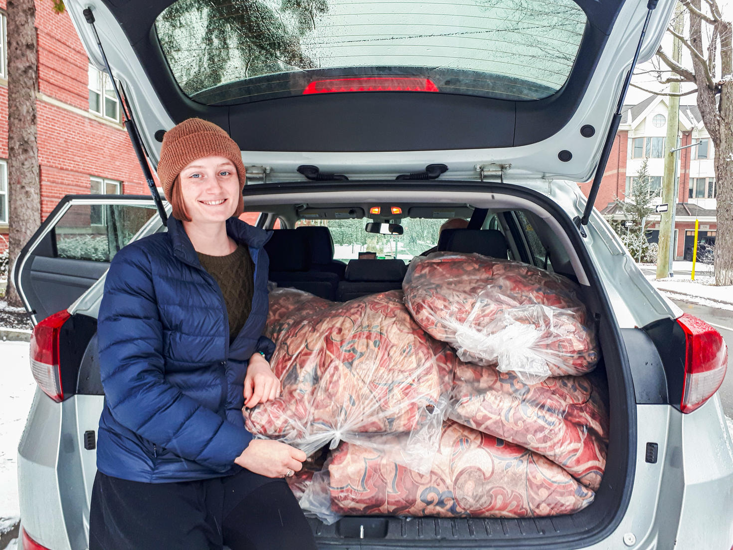 A student stands near the trunk of a vehicle full of donated blankets