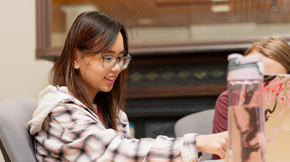 Une étudiante est assis à une table, en train de travailler.