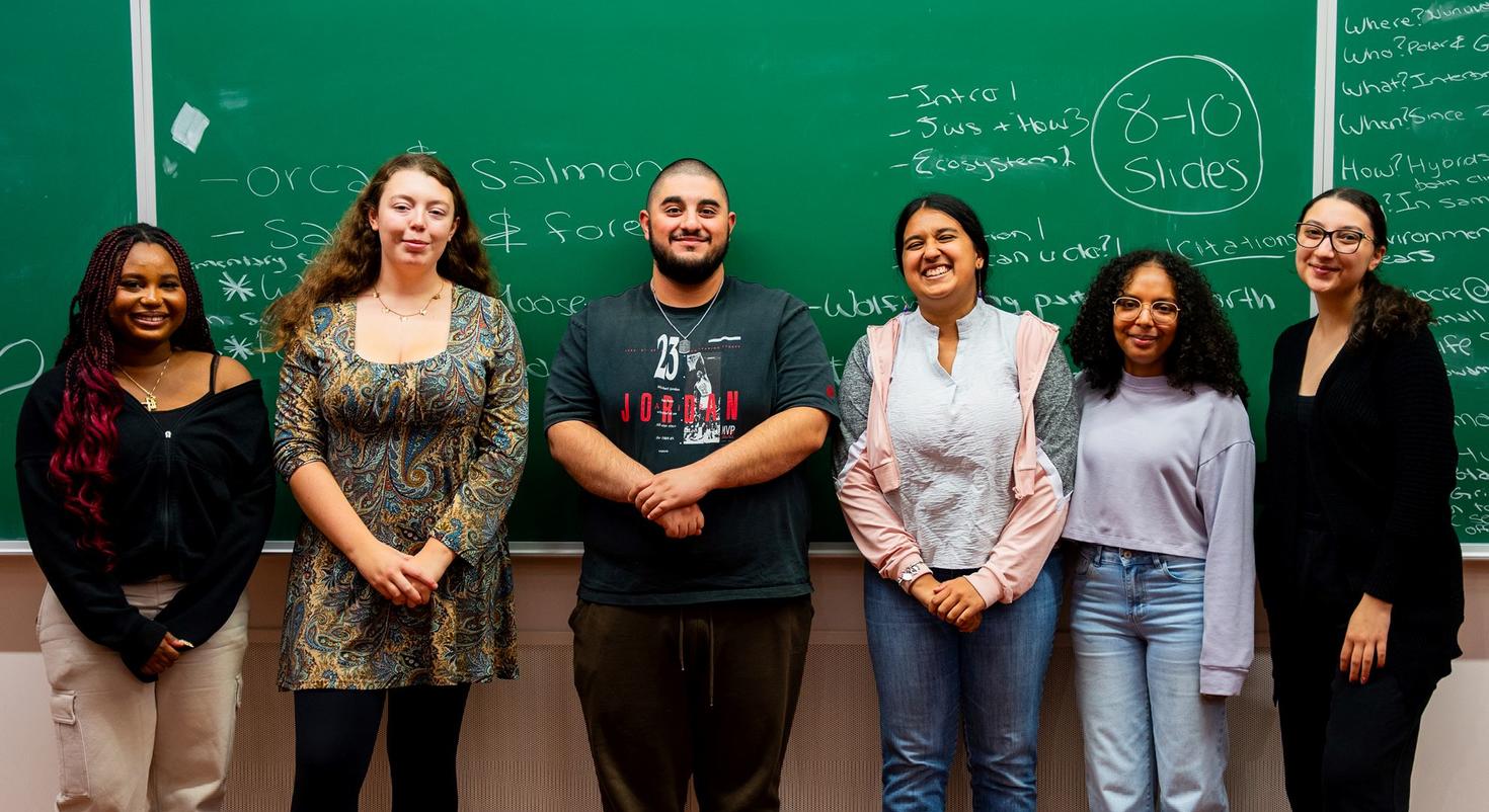 Six étudiantes et étudiants ayant participé en 2025 à un défi d'apprentissage expérientiel interdisciplinaire organisé par la Faculté des sciences sociales se tiennent devant un tableau noir dans une salle de cours.