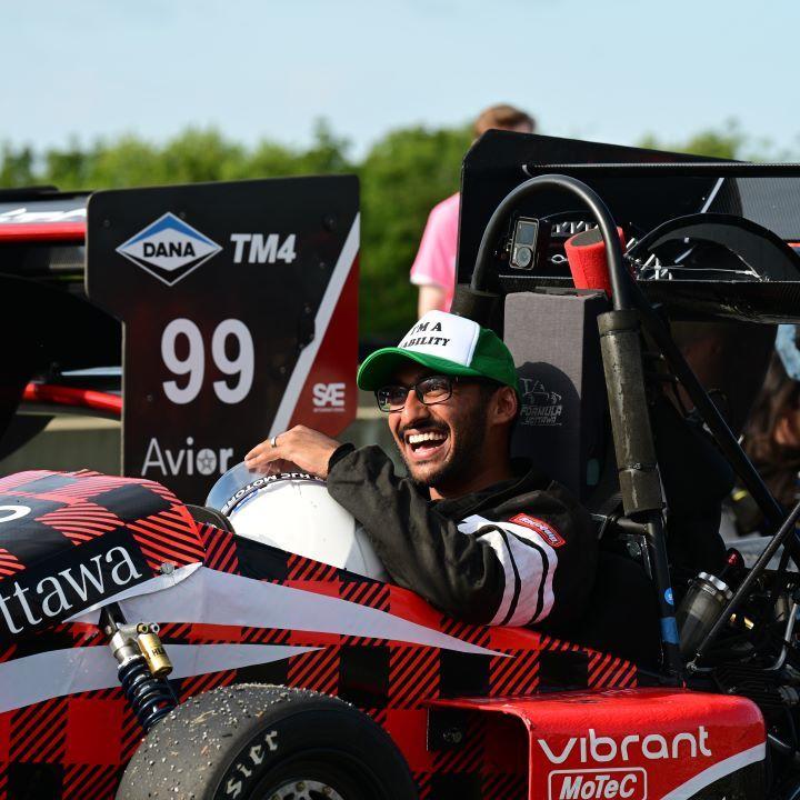 Faran Rashid, directeur technique de Formula uOttawa, est assis dans la voiture de course et sourit.